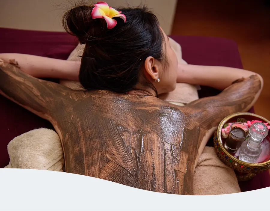 Asian woman receiving a back mud application at Pause Spa
