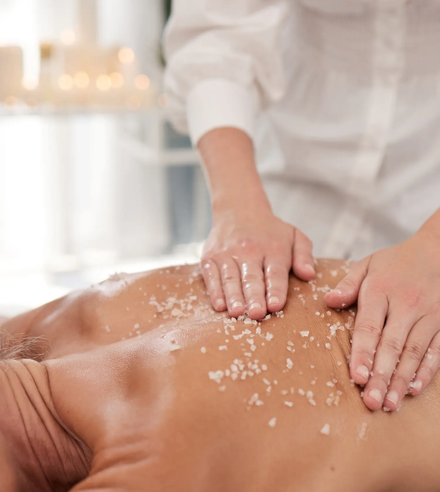 Woman receiving a body scrub treatment at Pause Spa, with therapist applying an exfoliating scrub to her back while she lies on a treatment bed