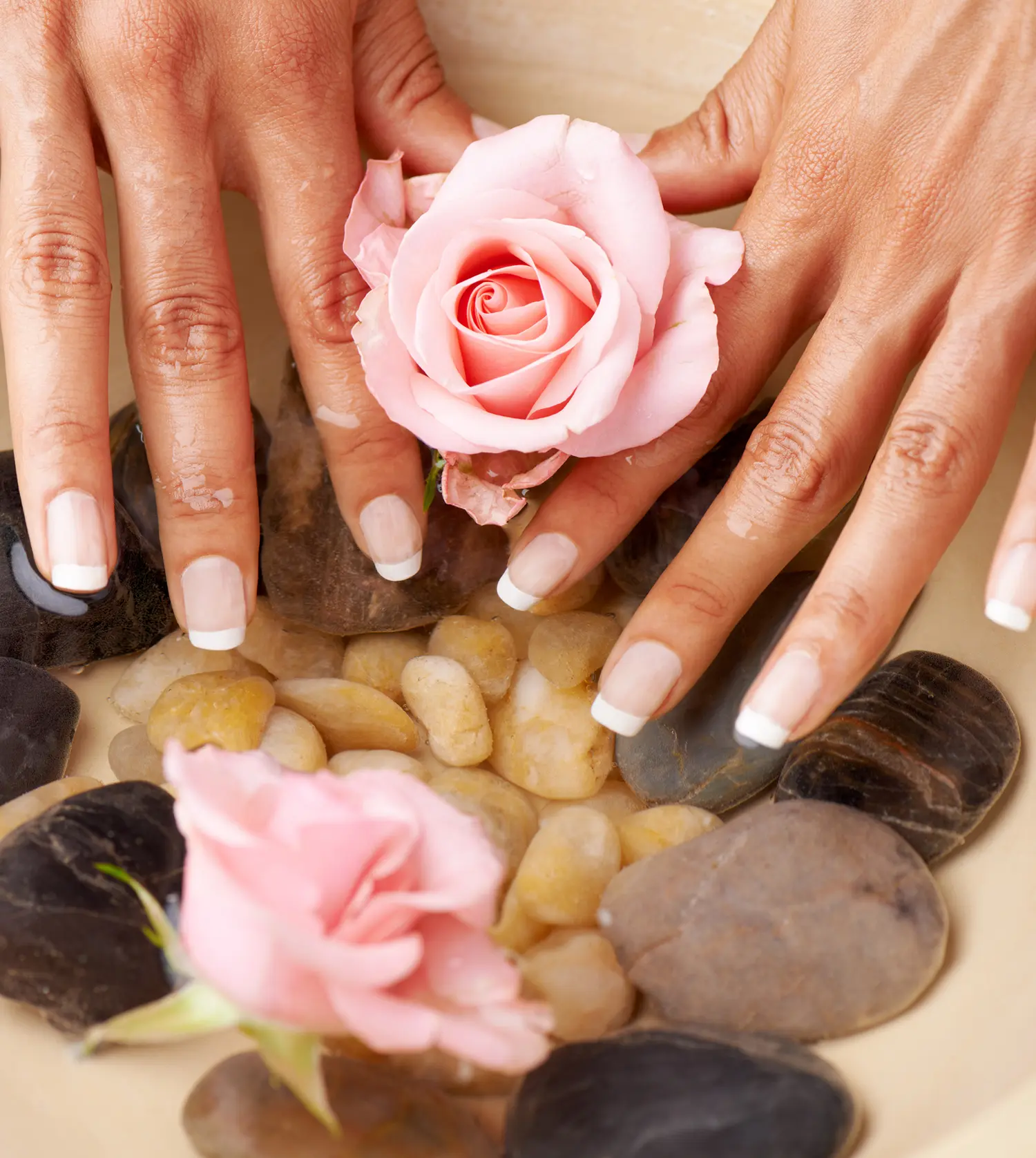 Woman soaking her hands in a bowl of water with flower petals during her Spa Manicure experience at Pause Spa