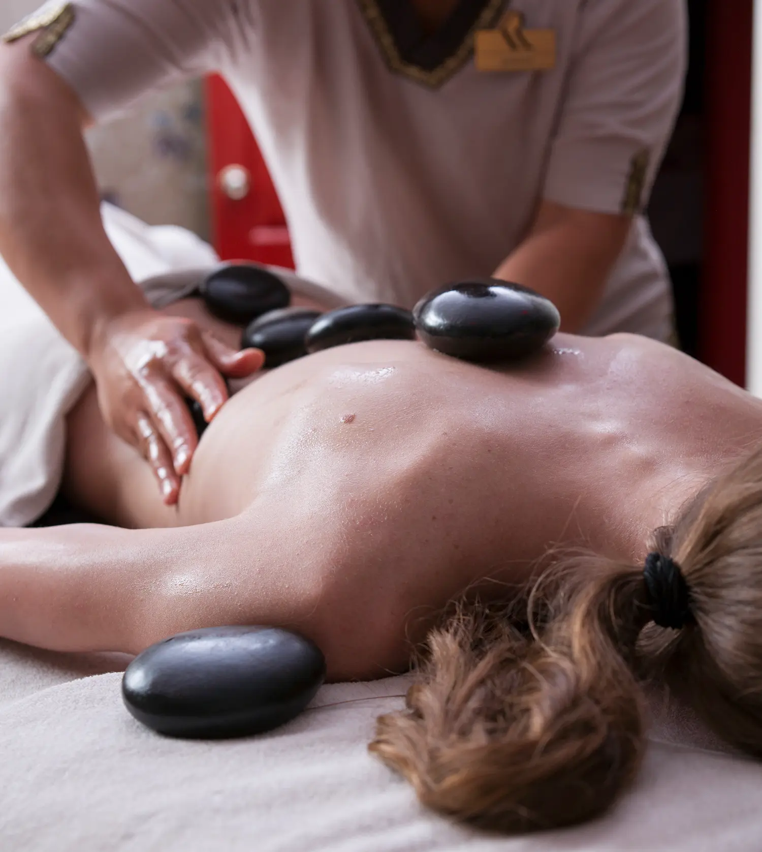 Therapist massaging a woman's ribs while hot stones are placed on her back during her Hot Stone Back Massage experience at Pause Spa